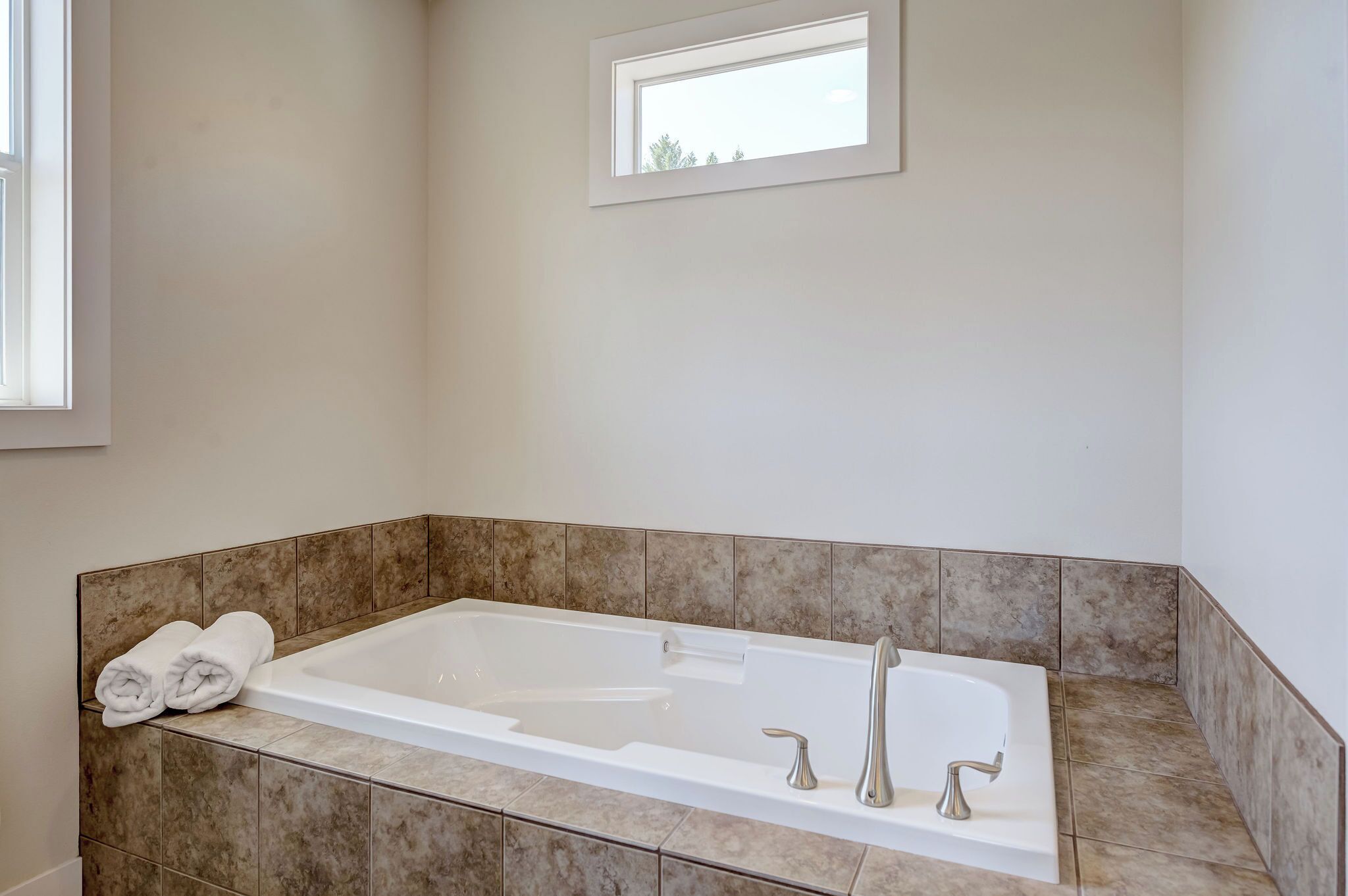 Un baño moderno con una bañera grande, una ventana pequeña y una toalla sobre el borde.
