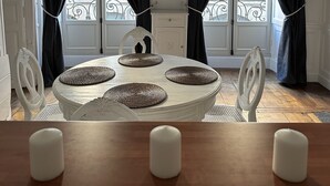A dining area with a round table, white chairs, and black curtains.