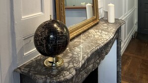 A marble fireplace with a gold-framed mirror above it, a globe on the mantel, and a hanging pendant light.