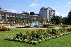A hotel with a large garden featuring a fountain, flower beds, and a lawn area.