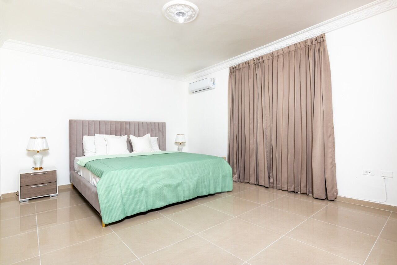 A neatly arranged bedroom with a bed, bedside tables, and an air conditioning unit.