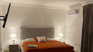 Une chambre à coucher bien rangée, avec un lit, deux tables de chevet dotées de lampes, un luminaire au plafond et un appareil de climatisation.