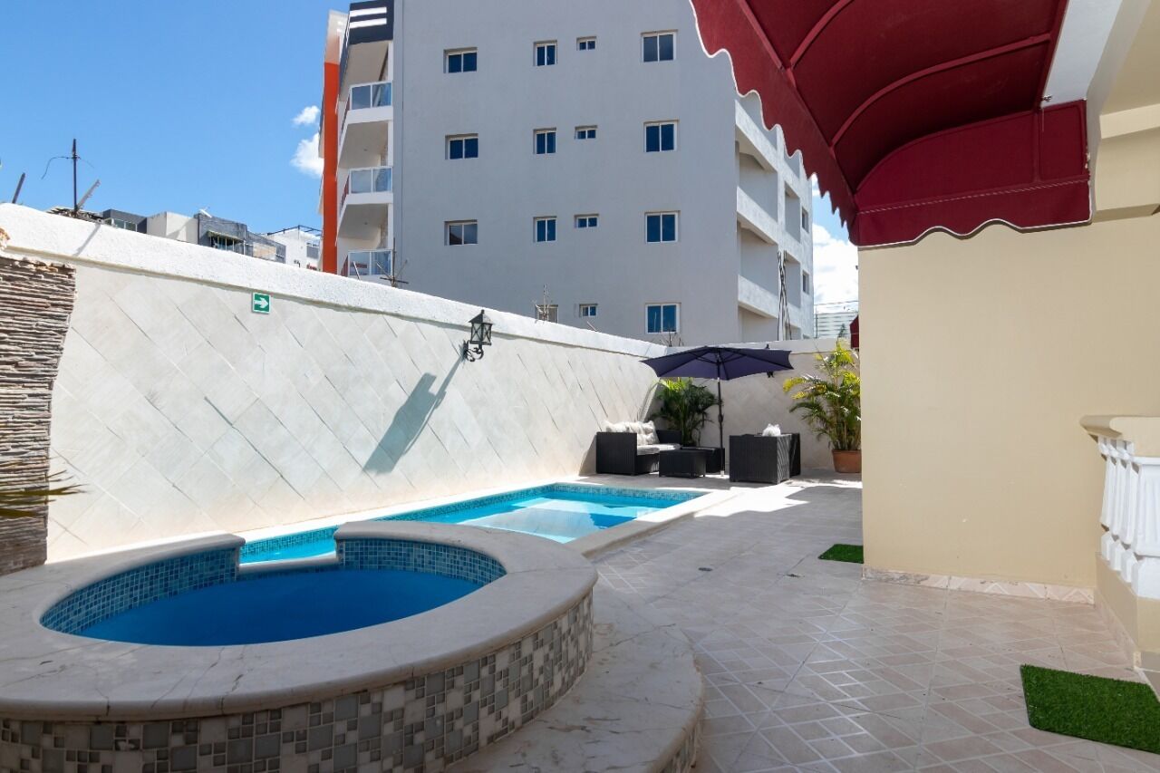Ein Poolbereich mit Whirlpool und Liegestuhl, umgeben von einer gefliesten Terrasse und einem Gebäude im Hintergrund.