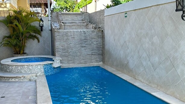Une piscine avec une terrasse carrelée, un petit jacuzzi et un mur en pierre.