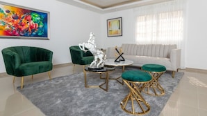 Un salon moderne avec un canapé vert, deux fauteuils verts, un canapé blanc et une table basse surmontée d’une statue argentée.