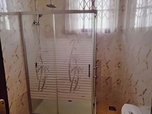 A bathroom with a glass shower enclosure, a toilet, and a marble-patterned wall. - Room-renajoe Ejisu-kubease (Kubease)