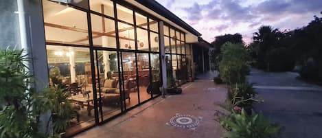 A building with large glass windows and doors, a tiled patio, and potted plants.