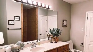 Un baño con tocador, lavamanos, espejo e inodoro.
