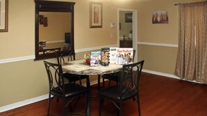Un coin repas avec une table dressée pour quatre personnes, entourée de chaises. On y trouve des boîtes de collations et un magazine.