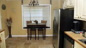 Une cuisine compacte comprenant une table à manger, des chaises, un réfrigérateur, une machine à café et un lave-vaisselle.