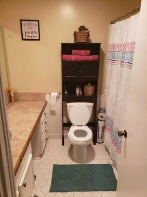 A bathroom with a toilet, a shelf with toiletries, a framed sign on the wall, and a shower curtain. - Lu's Home Away from Home (Jackson)