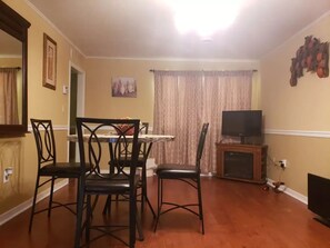 A dining area with a table and four chairs, a television on a stand, and a curtain. - Lu's Home Away from Home (Jackson)