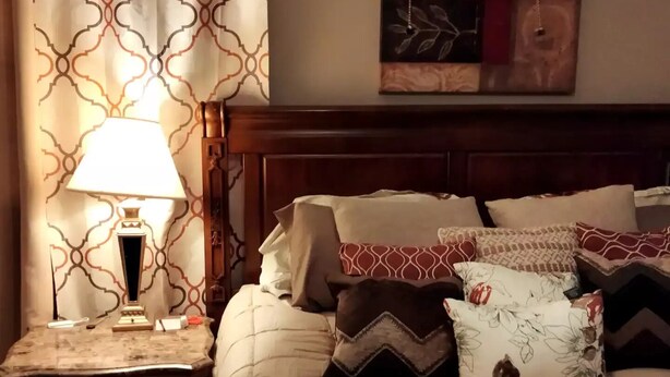 Un lit bien fait, agrémenté de plusieurs oreillers, et une table de chevet avec une lampe.