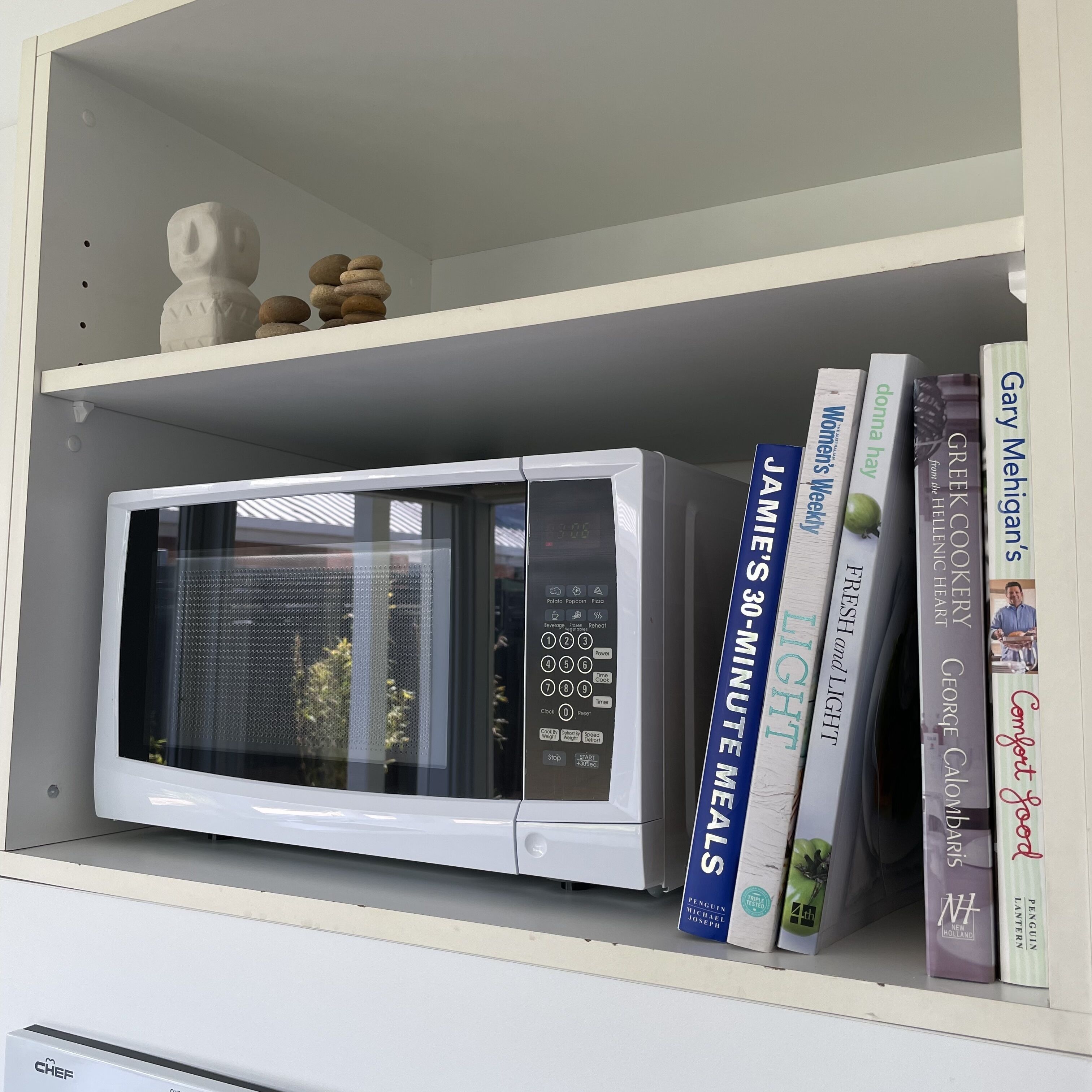 Una cocina con un microondas blanco, una repisa con libros y una decoración de piedras.