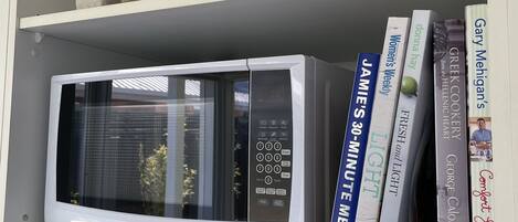 Una cocina con un microondas blanco, una repisa con libros y una decoración de piedras.