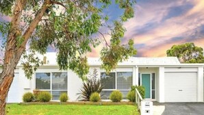 A single-story building with a flat roof, a front door, and a garage door. There are small shrubs and a large plant in the front yard. - Family & Pet Friendly - Only 1 Block From The Beach & Flying Fox Playground (Torquay)