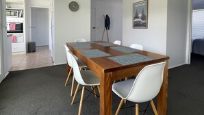 A dining area with a wooden table and white chairs, a clock on the wall, and a framed picture of Torquay. - Family & Pet Friendly - Only 1 Block From The Beach & Flying Fox Playground (Torquay)