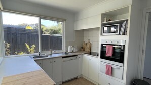 A kitchen with white cabinets, a wooden countertop, a microwave, an oven, and a window with a view of a fence and trees. - Family & Pet Friendly - Only 1 Block From The Beach & Flying Fox Playground (Torquay)