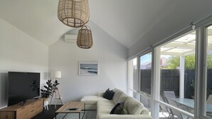 A modern living room with a sectional sofa, a coffee table, a TV, and a large window offering a view of the outdoors. - Family & Pet Friendly - Only 1 Block From The Beach & Flying Fox Playground (Torquay)