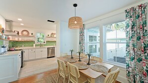 Una cocina moderna con armarios blancos, una mesa de comedor de madera con individuales tejidos, sillas de mimbre y una lámpara colgante.