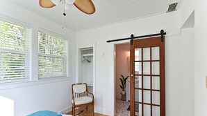 Una habitación con cama, una silla, una puerta corrediza y un ventilador de techo.