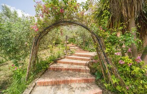 A stone pathway leading through a lush garden with a vine-covered archway.