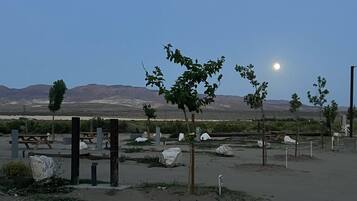 Een parkeerplaats met picknicktafels en enkele bomen, omringd door een kaal landschap en bergen in de verte.
