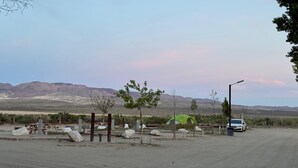 Paesaggio desertico con una tenda verde, un'auto bianca e un tavolo da picnic.