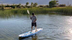Una persona in piedi su una tavola da paddleboard in acque limpide, con montagne sullo sfondo.
