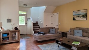 Una sala de estar con un sofá, una mesa de centro y una estantería. Hay una escalera que lleva a otra habitación.