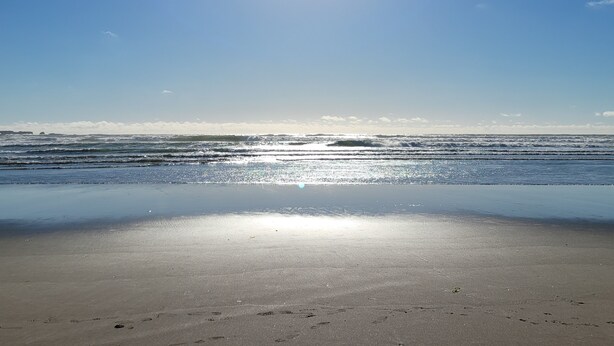 Una playa con cielo despejado y reflejos de sol en el agua.