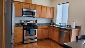Una cocina con gabinetes de madera, electrodomésticos de acero inoxidable, encimera de granito y una ventana con persianas.