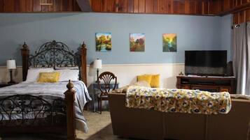 Quarto com cama, sofá, televisão e obras de arte nas paredes.