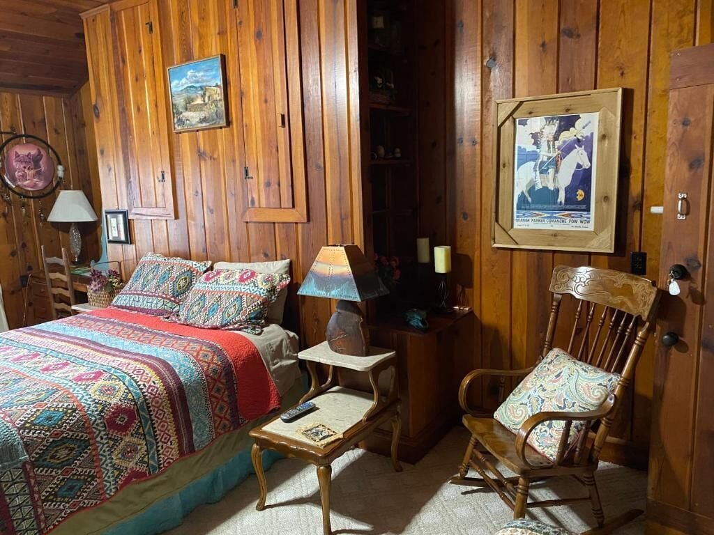 A cozy room with a bed, a chair, a small table, and a wooden door.