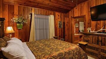 Un dormitorio con paneles de madera, una cama, un televisor y una cabeza de venado montada.