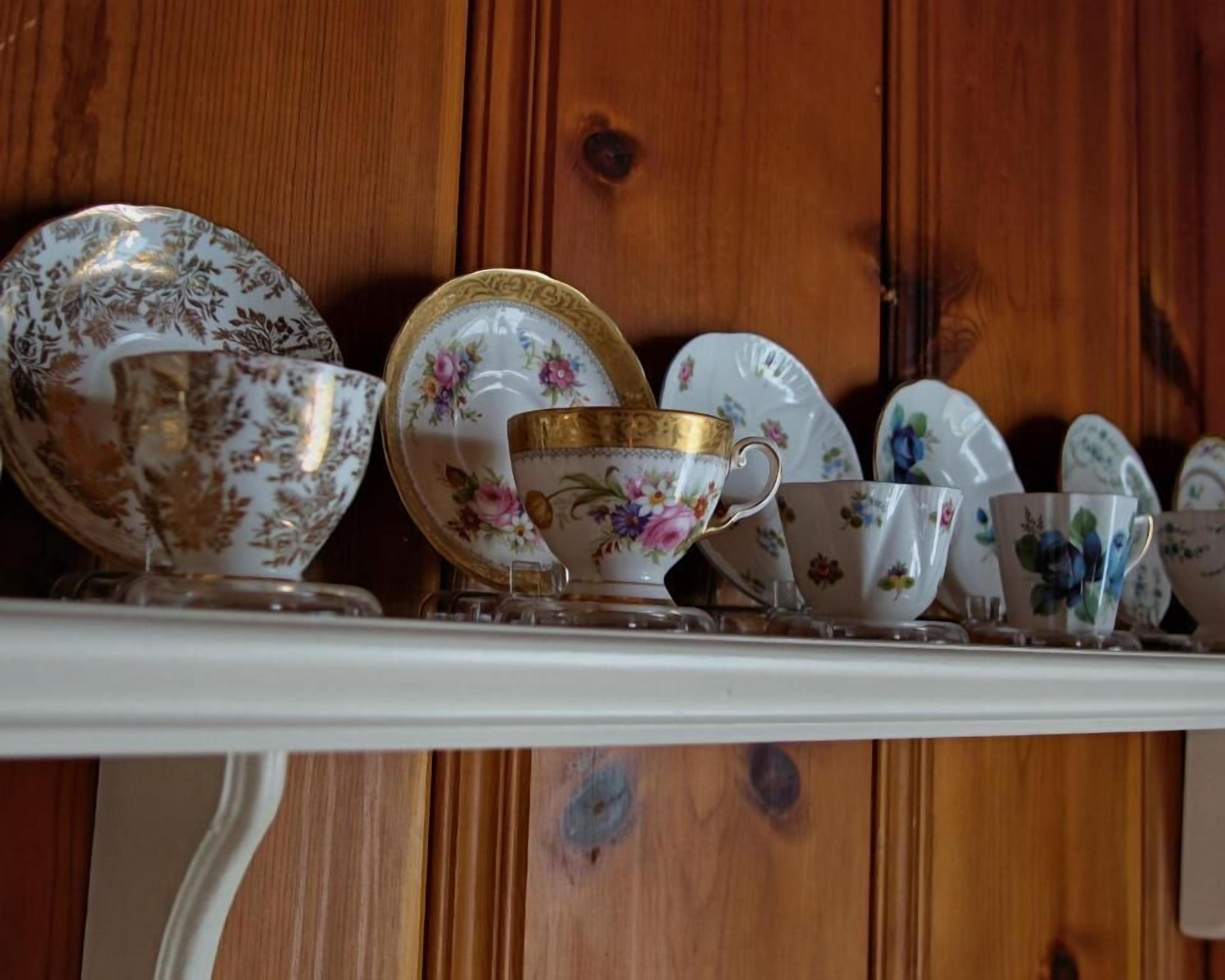 Une collection de tasses et de soucoupes en porcelaine ancienne, disposées sur une étagère devant un mur en bois.