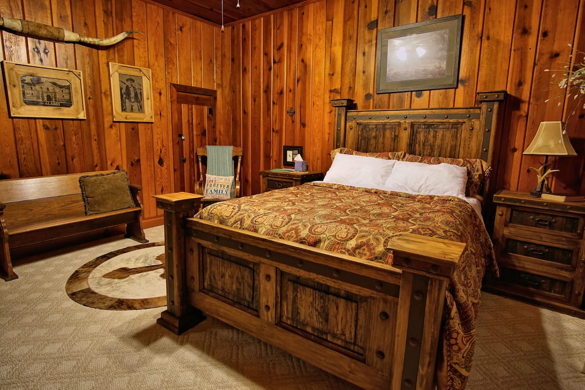 A wooden-themed bedroom with a large bed, a wooden bench, a nightstand, and a framed picture on the wall.