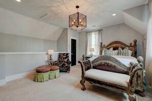 Een slaapkamer met een groot bed, een stoel, een klein tafeltje en een hanglamp.