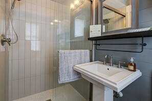 Een badkamer met een douchecabine van glas, een wit wastafelmeubel met zeepdispenser en een handdoekrek met een decoratieve handdoek.
