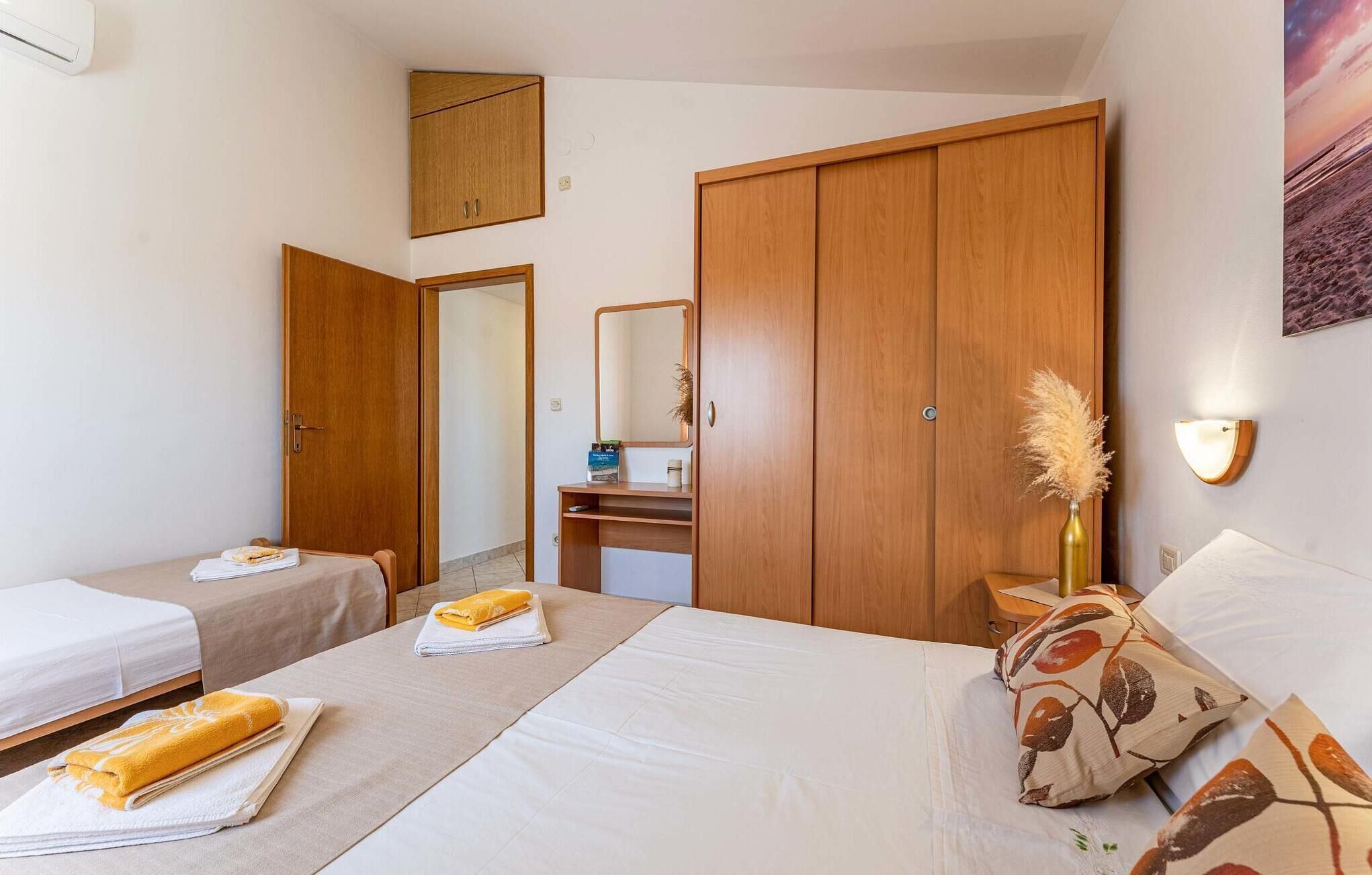 A hotel room with two beds, a wardrobe, a vanity with a mirror, and a wall-mounted lamp.