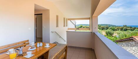 A balcony with a wooden table set for breakfast, a view of greenery and a distant landscape.