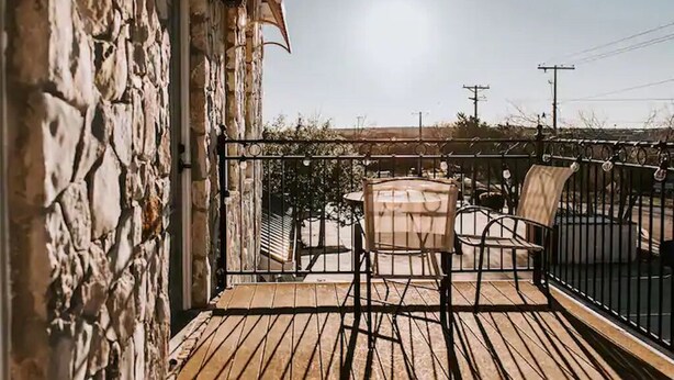 A wooden deck with a stone wall, a table, and two chairs. - GrueneGusthaus#3| Private Condo+ Golf Cart Rentals (New Braunfels)