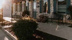 A stone building with a stone facade, green shutters, and a bench in the foreground. - GrueneGusthaus#3| Private Condo+ Golf Cart Rentals (New Braunfels)