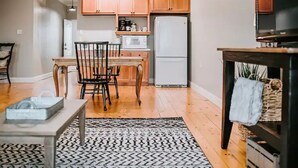 A modern kitchen with wooden cabinets, a white refrigerator, and a dining area with a table and chairs. - GrueneGusthaus#3| Private Condo+ Golf Cart Rentals (New Braunfels)