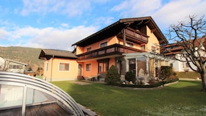 A two-story house with a balcony, a covered patio, and a well-maintained lawn. - Comfortable Apartment Near Nassfeld (Hermagor-Pressegger See)