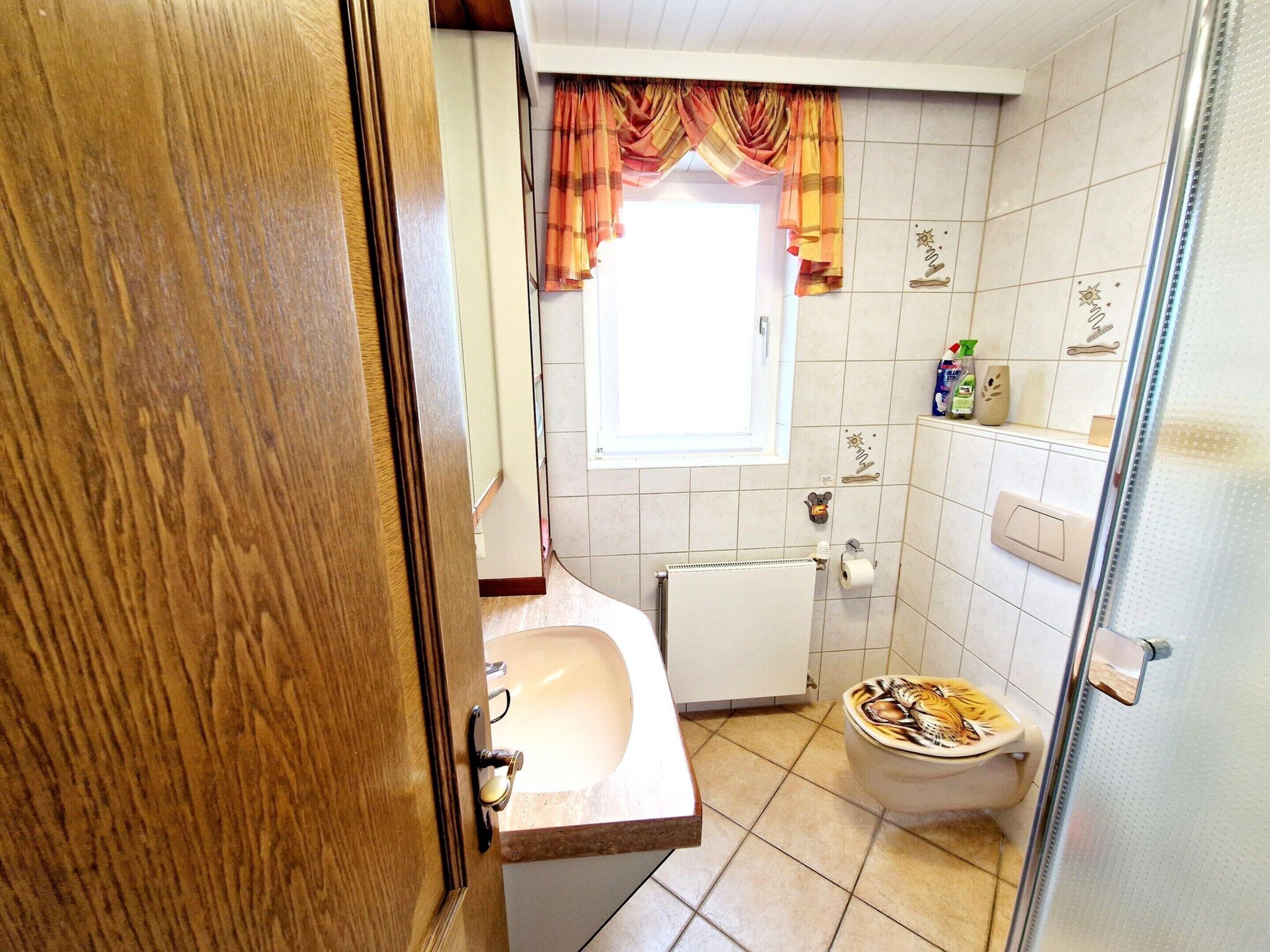 A bathroom with a toilet, sink, and a window with curtains.