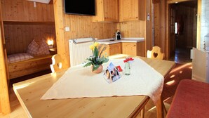 A cozy wooden cabin interior with a dining table set for two, a television mounted on the wall, and a small kitchen area. - Comfortable Apartment Near Nassfeld (Hermagor-Pressegger See)