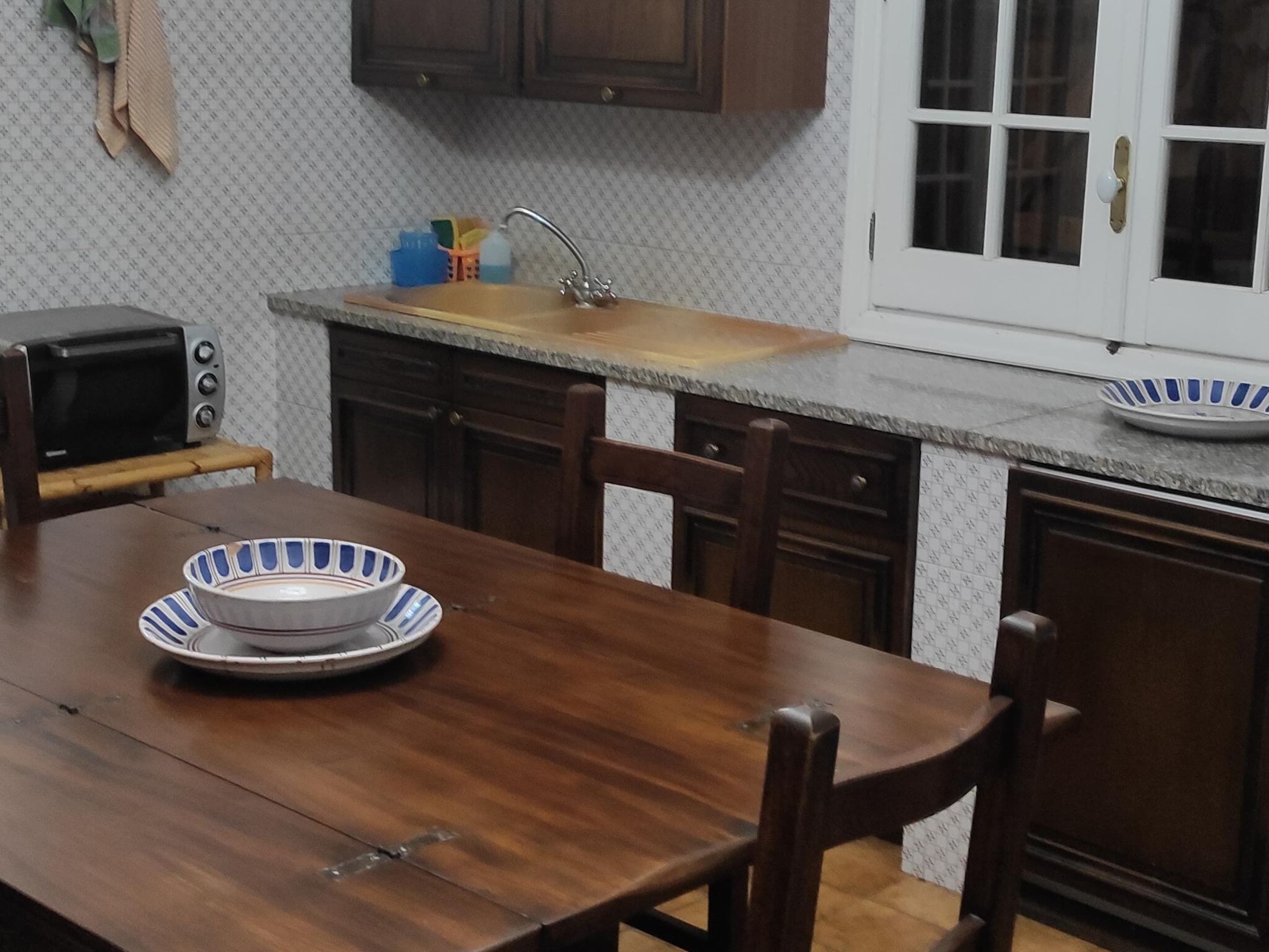 A kitchen with wooden cabinets, a countertop, a sink, a toaster, and a dining table with a bowl and plate.