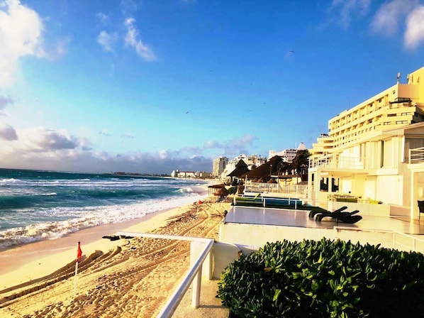 A beachfront hotel with a pool, ocean view, and a beach area with umbrellas.