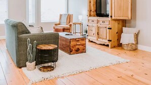 Een woonkamer met een bank, fauteuil, houten kast met een televisie, een klein rond tafeltje en een cactus.